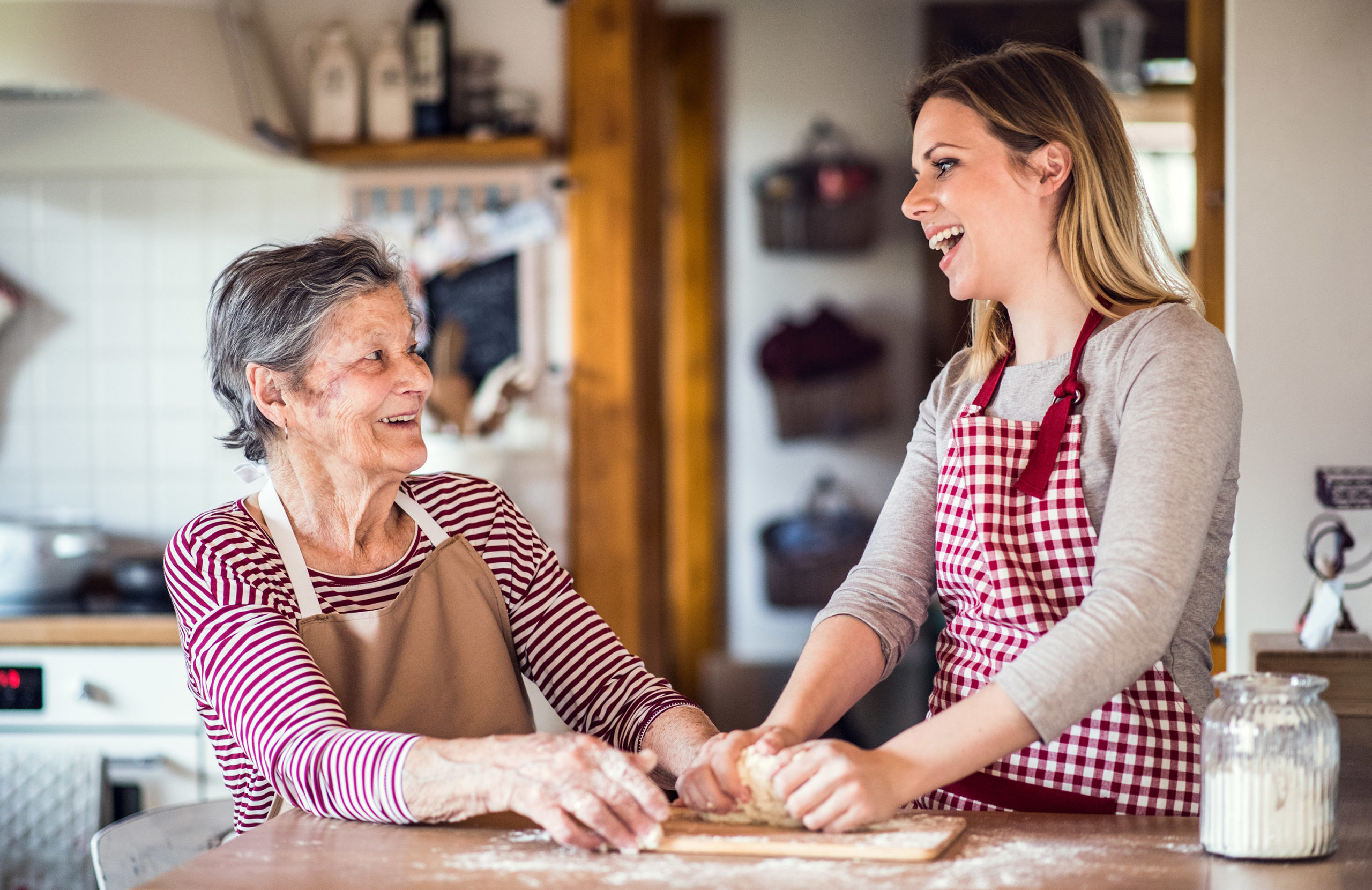 A happy elderly grandmother with an adult granddaughter at home, baking.